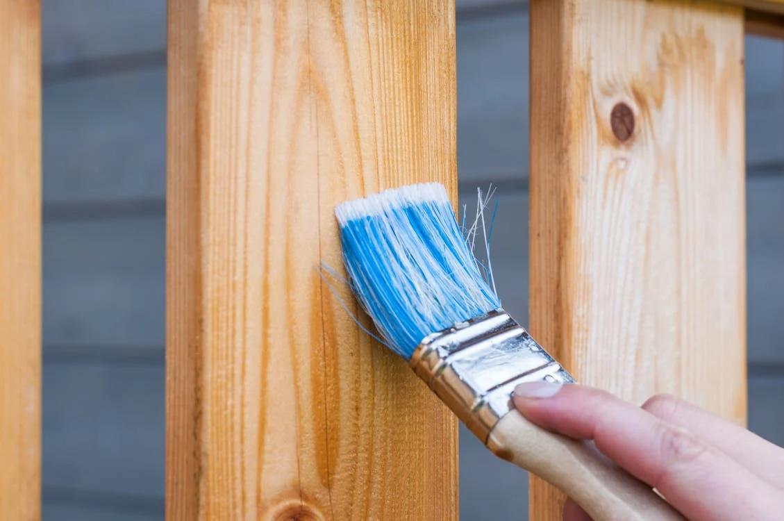 Individual painting a backyard fence, emphasizing the importance of preparation in fence installation.