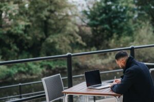 Man working outdoors on a laptop beside a river with a commercial fence in Camden County
