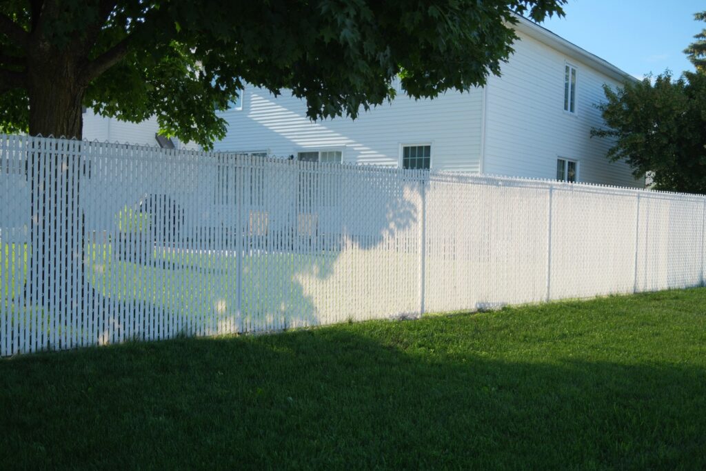 Homeowner rinsing white vinyl fence with garden hose in Sicklerville, NJ