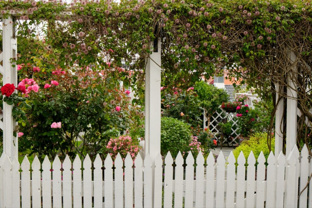 a white picket fence running along a garden full of colorful flowers